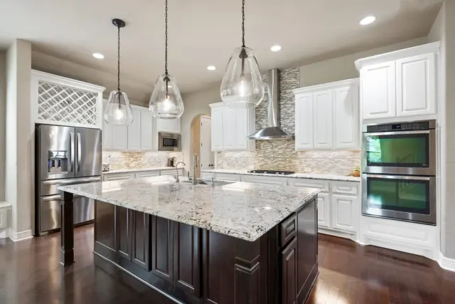 White kitchen with a granite-topped island and dark hardwood flooring.